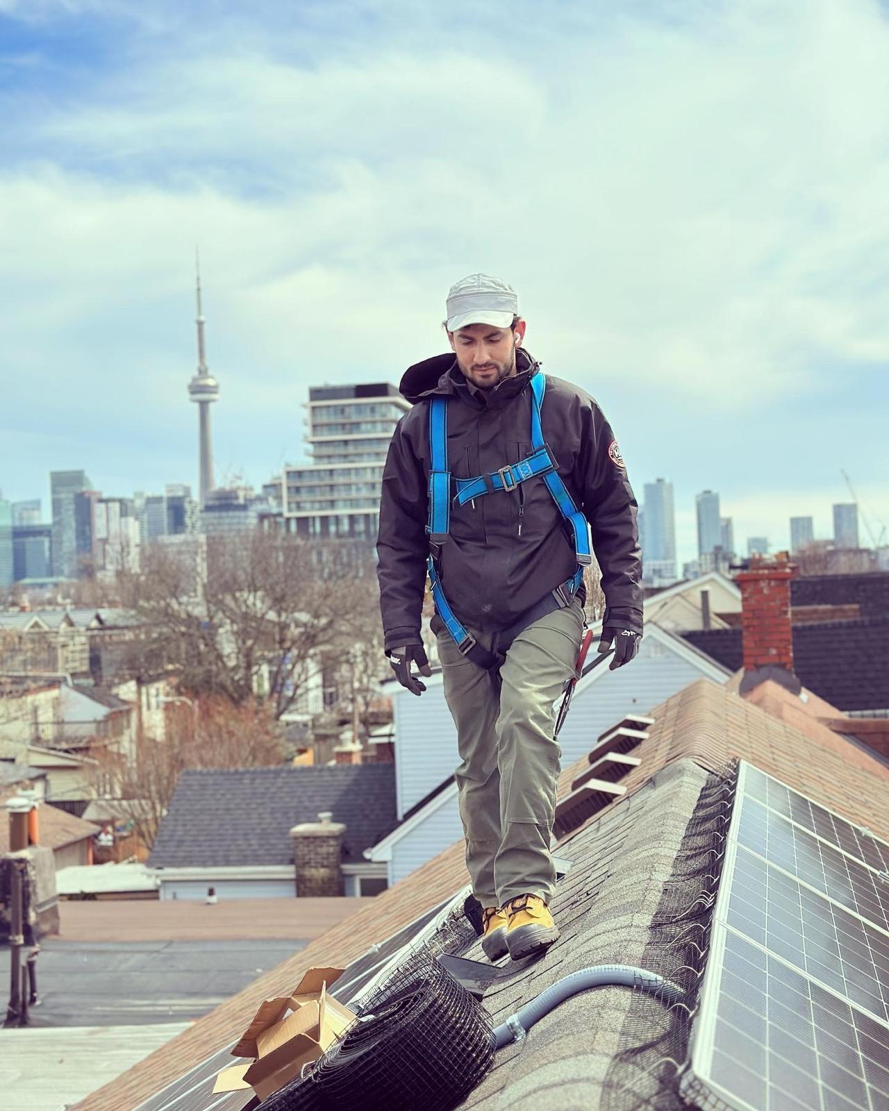 Ronahi Solar installer in a safety harness on a Toronto rooftop solar install, with the CN Tower behind