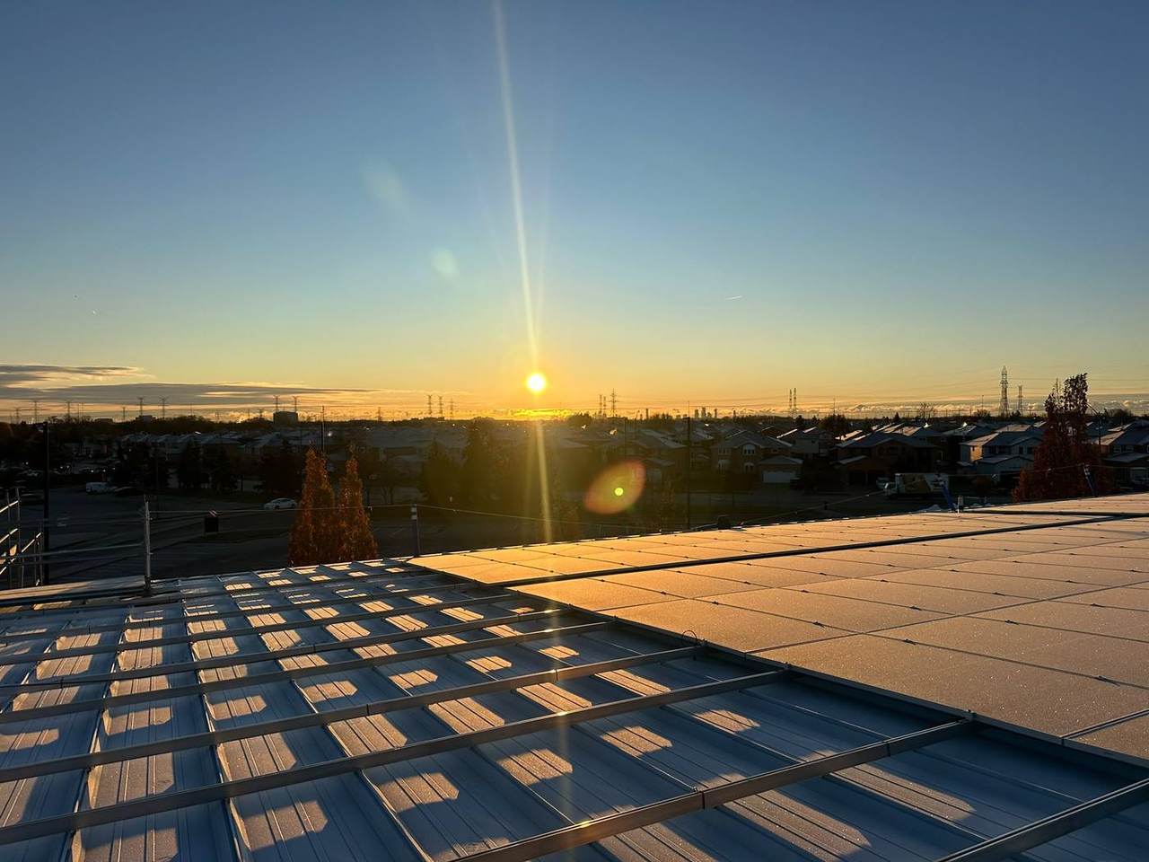 The sun setting behind rows of solar panels on a commercial roof